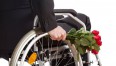Na zdjęciu osoba na wózku inwalidzkim z bukietem róż 