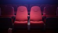 Zdjęcie przedstawia puste, czerwone fotele w sali kinowej