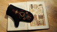 Zdjęcie przedstawia filcową rękawicę leżącą na książce z ilustracjami wzorów  jamneńskich.