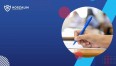 Na grafice znajduje się ręka trzymająca długopis