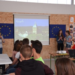 Zdjęcie przedstawia uczniów w sali lekcyjnej. Na ścianie widnieje tablica korkowa. Uczniowie z Koszalina prezentują miasto Koszalin. Pośrodku zdjęcia na rzutniku wyświetlony jest slajd na którym widać koszalińską Katedrę.