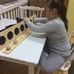 obrazek w kolorze ukazuje dziewczynkę z kitką siedząca przy stoliku i zajętą zabawką dydaktyczną ( zajęcia w SOSW1)