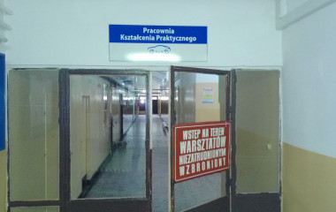 Zdjęcie drzwi wejściowych do pracowni kształcenia praktycznego. Drzwi zlokalizowane są w korytarzu placówki szkolnej.