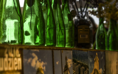 Zdjęcie przedstawia szklane, zielone butelki, przez które przechodzi światło słoneczne