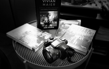 Dyskusyjny Klub Fotograficzny - „W świetle fotografii” Czarno białe zdjęcie przedstawia aparat fotograficzny leżący na stoliku w towarzystwie książek.