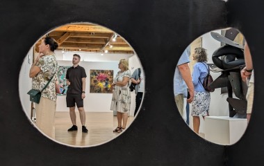 Zdjęcie przedstawia ludzi zwiedzających wystawę, widocznych przez dwa duże otwory umieszczone na czarnym tle.