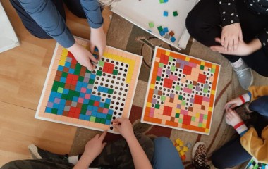 obrazek w kolorze ukazuje czworo dzieci - widok z góry - bawiące się kolorowymi puzzlami