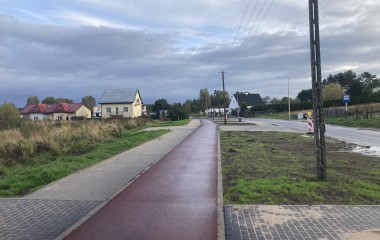Obrazek ukazuje część ulicy Dzierżęcińskiej w Koszalinie: od lewej widok na domki i chodnik dla pieszych, obok nowa droga rowerowa, w głębi domy, po prawej stronie jezdnia 