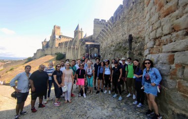 Obrazek w kolorze ukazuje grupę młodych osób, uczestników projektu stojących na wzgórzu, w tle mury i zamek