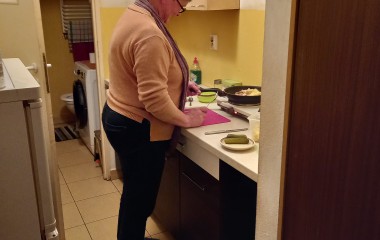zdjęcie przedstawia opiekunkę podczas wykonywania usług opiekuńczych - opiekunka stoi w kuchni i przygotowuje obiad dla podopiecznego